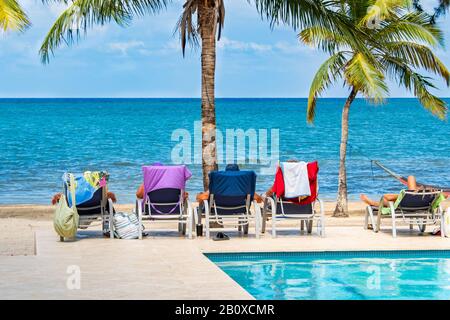 People relaxing on lounge chairs between a pool and tropical beach on a beautiful day. Stock Photo