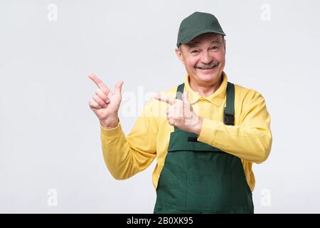 Smiling senior worker looking at camera and pointing aside with index finger. Studio shot Stock Photo