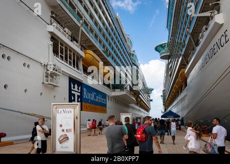 Tourists on vacation walk to and from their cruise ships at port; 'Royal Caribbean International' cruise ship logo viewable in distance Stock Photo