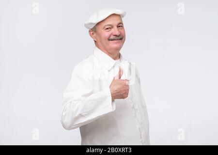 Happy senior hispanic chef with thumbs up isolated on white wall, studio shot Stock Photo