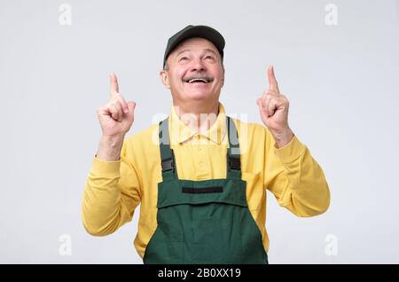 Smiling senior worker looking at camera and pointing up with index finger. Studio shot Stock Photo