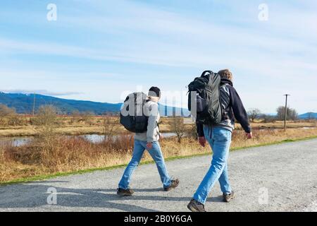 Male and female walkers with backpacks along a dike trail in Pitt Meadows, B. C., Canada.  Stock photo. Stock Photo