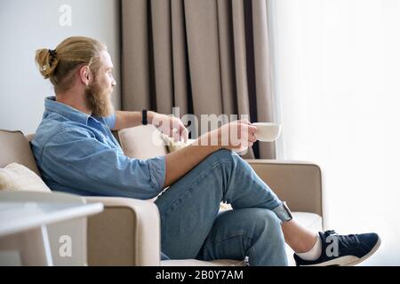 Happy serene young man relax on comfortable sofa holding coffee cup Stock Photo