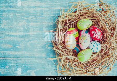 Easter eggs in various patterns and colors in a bird's nest placed on a wooden floor decorated in retro style. Stock Photo