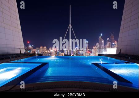 Pool on the roof of a skyscraper in Jumeirah Lakes Towers (JLT) at night with a view of the skyline, New Dubai, United Arab Emirates, Stock Photo