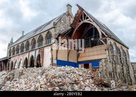 A gothic church being demolished. The walls facing the viewer are missing and the interior is visible. Lots of rubble in front. Overcast sky. Stock Photo