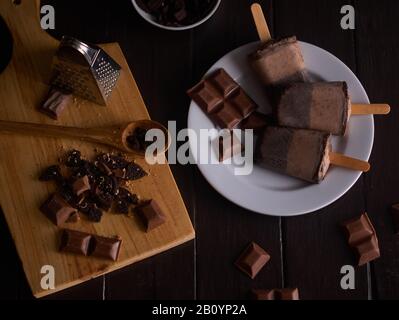 Chocolate and cookie ice cream on white ceramic cup and chocolate chip on wooden cutting board with chocolate pieces and cookie pieces Stock Photo
