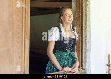 Farmer with dirndl looks out of the stable door Stock Photo