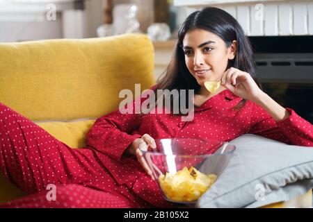 Persian woman at home watching TV eating chips potatoes Stock Photo