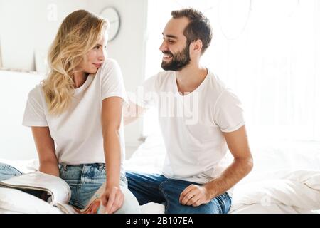 Happy young couple in love relaxing on a couch at the living room, reading magazine, laughing Stock Photo