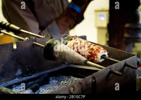 Cone pizza being autoatically turned on a stick kebab over an open oven filled with sticks on fire Stock Photo