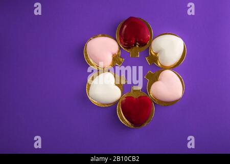 Modern mousse cakes with red, pink and white mirror glaze in the shape of a heart on purple background. Valentine's day background. Wedding cake. Roma Stock Photo