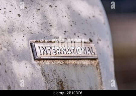 Old worn chrome plate with engraving "INTERNATIONAL" on it. The plate on a rusty metal surface with spots of mold and moss on it. Stock Photo
