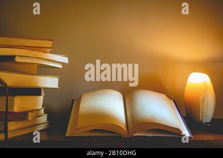 An old open book with blank pages on a candle lit table next to a stack of books - Education and leisure concept image with copy space for text. Stock Photo