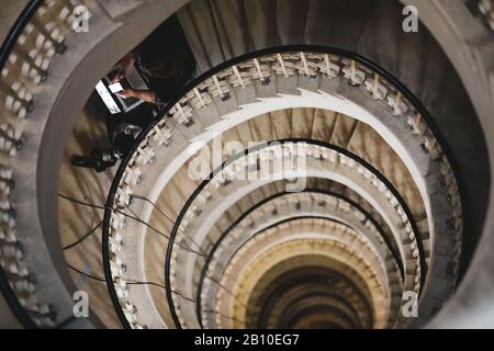 Shallow depth of field (selective focus) image with a woman journalist using her laptop and mobile phone on a very deep spiral staircase Stock Photo