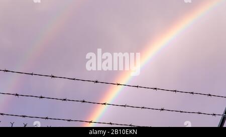 Double rainbow behind rows of barbed wire against cloudy sky Stock Photo