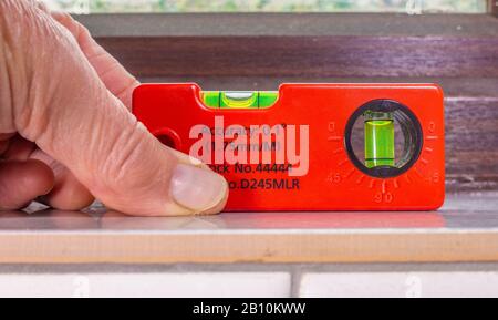 Close POV shot of a man’s hand checking the horizontal accuracy of window tiling with a spirit level / bubble level. Stock Photo