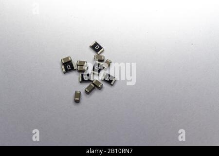 Abstract close-up of grey scattered 0603 SMT surface mount chip MLCC capacitors and 1206 resistors power electronics components on white background in Stock Photo