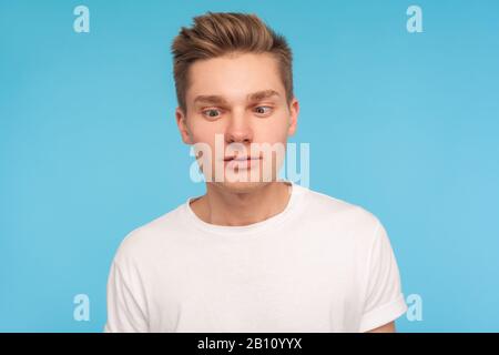 Portrait of funny comic young man in casual white t-shirt looking cross-eyed with awkward silly dumb expression, having fun alone, playing fool. indoo Stock Photo