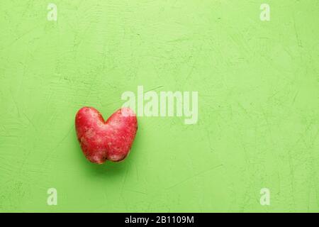 Ugly potato in the heart shape on a green concrete plaster background. Vegetable or food waste concept. Top view, close-up. Stock Photo
