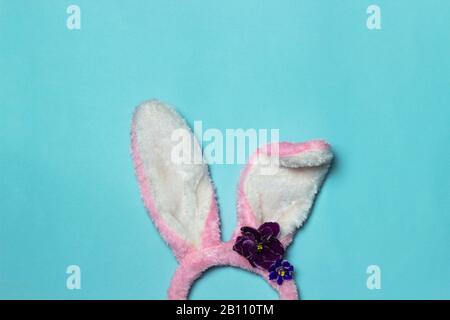 Pink bunny ears headband with violets on blue background. Easter concept. Copy space, top view.er or spring backdrop for banners, greeting cards. Stock Photo
