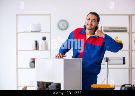 The young male contractor repairing refrigerator at workshop Stock Photo