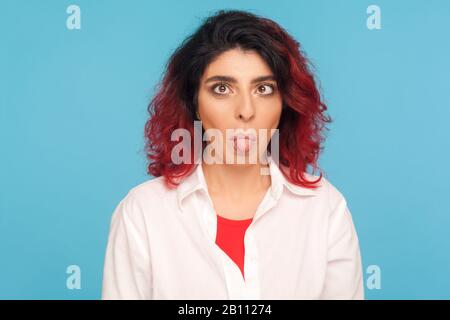 Portrait of silly dumb hipster woman with fancy red hair doing crossing eyes and sticking out tongue, foolishing with stupid brainless expression. ind Stock Photo