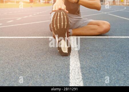 Close up of young man runner stretching legs before run - workout concept