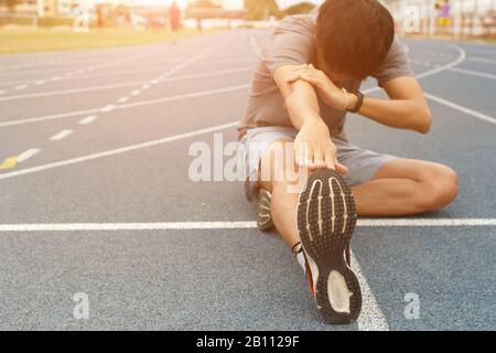 Young man runner stretching legs before run - workout concept