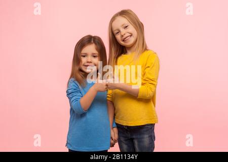 Children showing like, approval sign. Two adorable happy little girls gesturing thumbs up together and smiling to camera, excellent feedback, good job Stock Photo