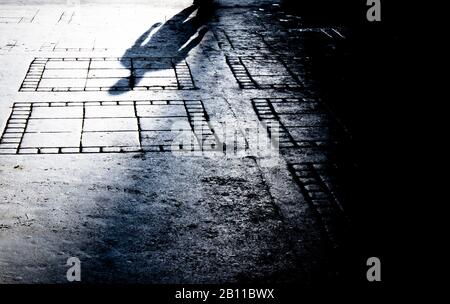 Blurry shadow silhouette of a man walking alone in the night on city street sidewalk in black and white Stock Photo