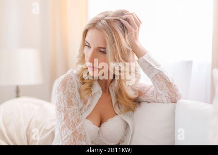 Young woman dreamily sits on sofa Stock Photo