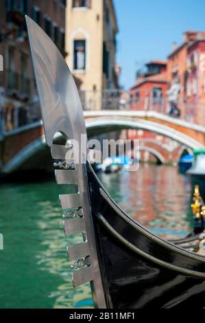 Close-up of a traditional 'ferro' metal bow on a Venetian gondola in front of a bright sunny canal view of Venice, Italy Stock Photo