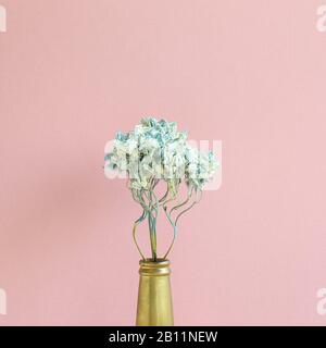 Dried blue hydrangea flower in golden bottle with pink background. Floral composition, copy space Stock Photo