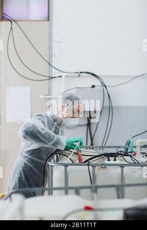 Young technician in protective clothing and in protective mask working with equipment in the factory Stock Photo