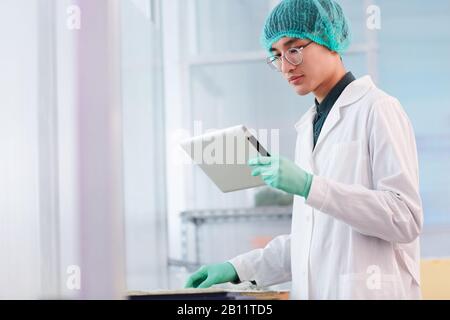 Asian young scientist in white coat standing and using digital tablet in his work in the laboratory Stock Photo