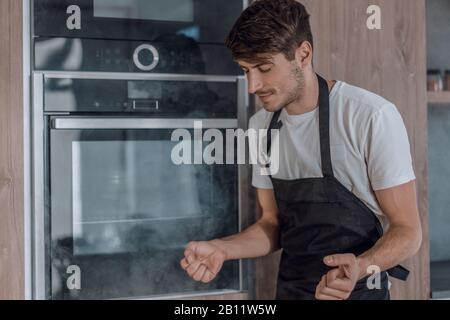 frustrated young man standing near broken oven Stock Photo