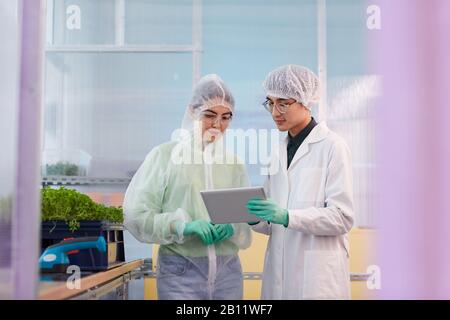 Young colleagues in protective workwear using digital tablet in the work while working in the lab Stock Photo