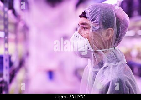 Side view of Asian chemist in protective clothing and in protective mask working with chemicals Stock Photo