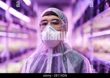 Portrait of Asian chemist in protective workwear and protective mask looking at camera Stock Photo
