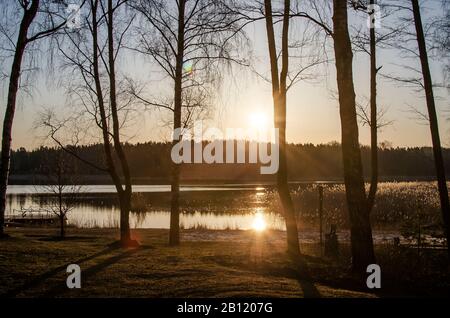 Sunrise on the lake in spring. Forest silhouettes and the rays of the rising sun. Stock Photo