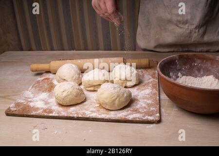 A woman kneads the dough. Plywood cutting board, wooden flour sieve and wooden rolling pin - tools for making dough. Stock Photo