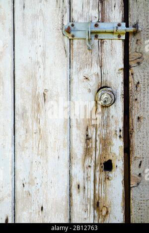 Old Yale cylinder lock in weathered, painted wooden door, reused as chicken shed door. Stock Photo