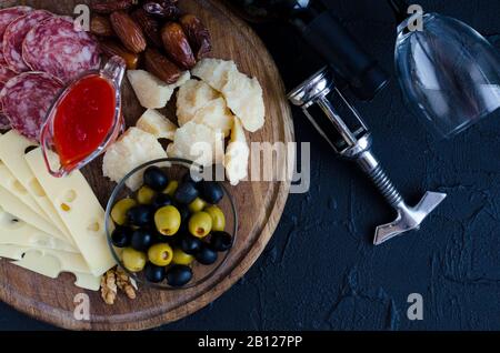 Bottle of wine with wine glass, corkscrew and antipasti on dark background. Wooden board full of mediterranean appetizers, tapas or antipasto. Assorte Stock Photo