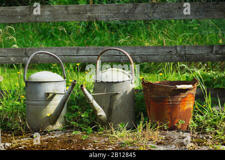 Two glavanised watering cans and a rusty galvanised bucket used to collect ashes from a coal fire. Shows the effect of acid water on metal. Stock Photo