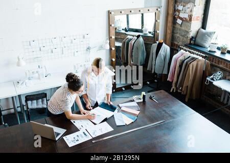 Two professional seamstresses or fashion designers discussing sketches of models Stock Photo