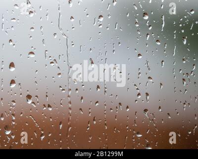 Rain drops on window glass surface with cloudy background . Natural Pattern of raindrops isolated on blurred background. Stock Photo