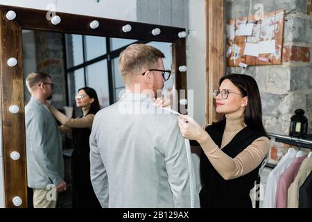 Young female tailor taking measures of jacket of young man in workshop Stock Photo