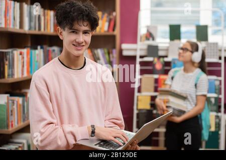 Smiling teenager in casualwear scrolling through list of books to read for exams Stock Photo