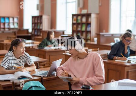 Two teenagers looking through books and online sources in college library Stock Photo